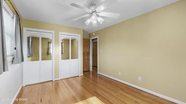 unfurnished bedroom with ceiling fan, multiple closets, and light wood-type flooring