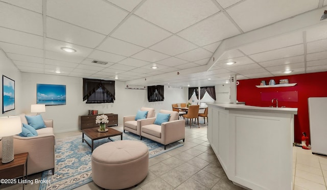 living room featuring light tile patterned flooring, a paneled ceiling, and bar area