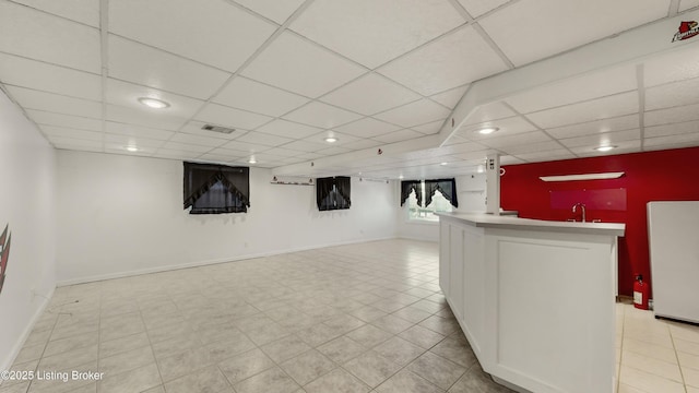 basement with fridge, a paneled ceiling, and indoor wet bar