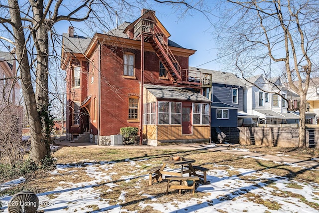 snow covered back of property featuring a balcony, a sunroom, and central air condition unit