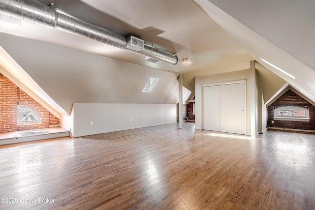 bonus room with brick wall, wood-type flooring, and lofted ceiling