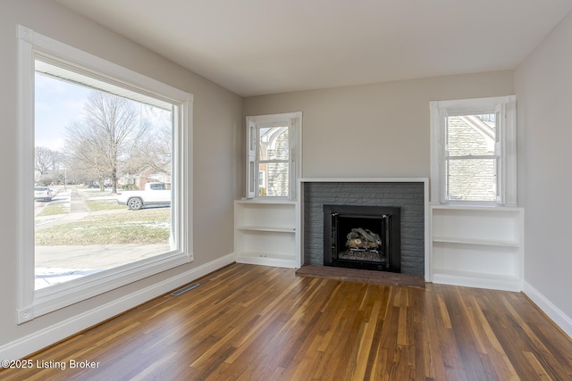 unfurnished living room featuring built in shelves, a fireplace, and dark hardwood / wood-style flooring