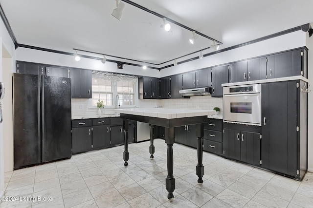 kitchen with sink, backsplash, tile counters, stainless steel oven, and black fridge