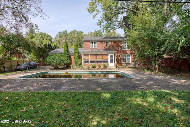 back of house with a fenced in pool, a sunroom, and a lawn