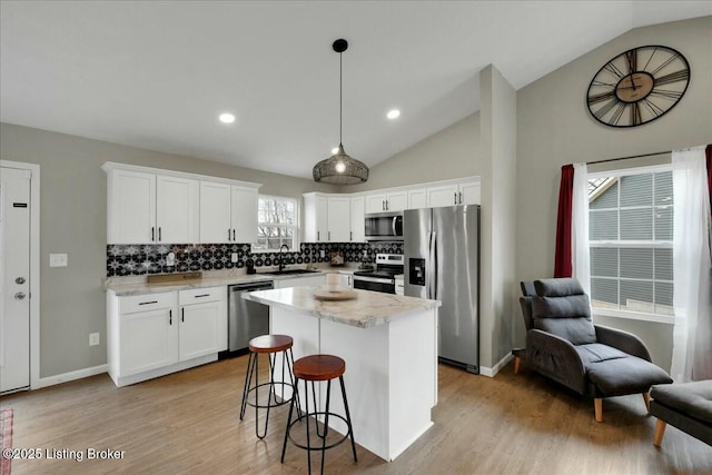 kitchen featuring a kitchen island, appliances with stainless steel finishes, white cabinetry, sink, and hanging light fixtures