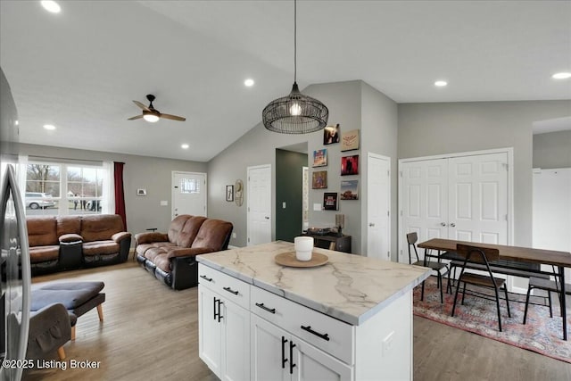 kitchen featuring white cabinetry, hanging light fixtures, a center island, light stone countertops, and light hardwood / wood-style floors