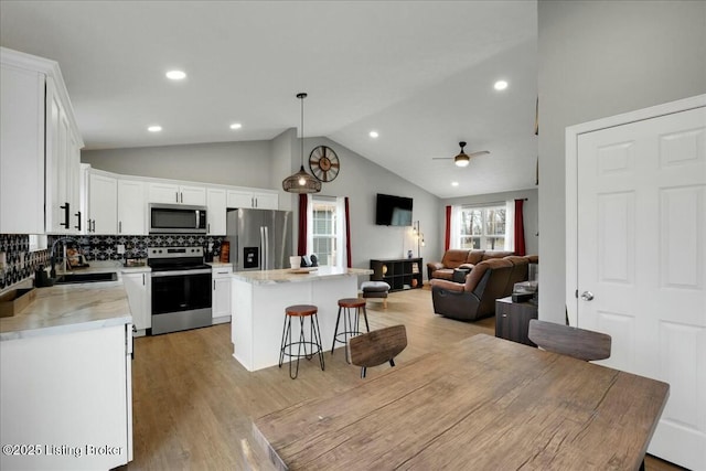 kitchen featuring a kitchen island, appliances with stainless steel finishes, decorative light fixtures, white cabinetry, and sink