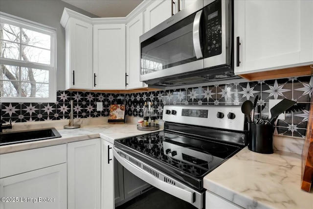 kitchen with sink, appliances with stainless steel finishes, white cabinets, light stone countertops, and backsplash