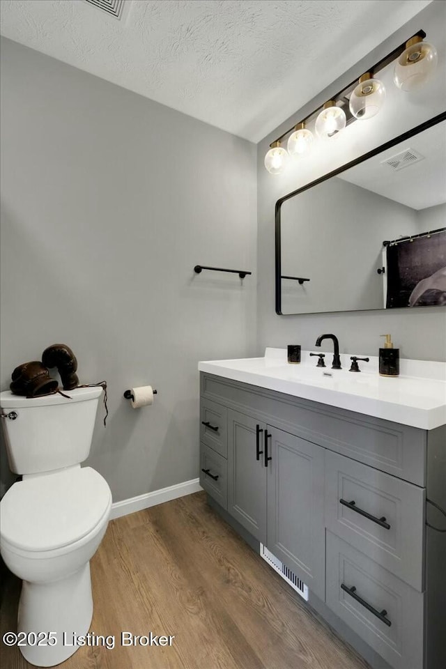 bathroom featuring hardwood / wood-style flooring, vanity, toilet, and a textured ceiling