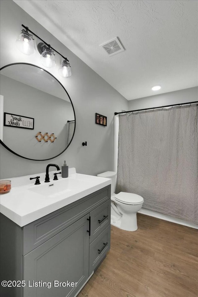 bathroom featuring curtained shower, wood-type flooring, vanity, toilet, and a textured ceiling