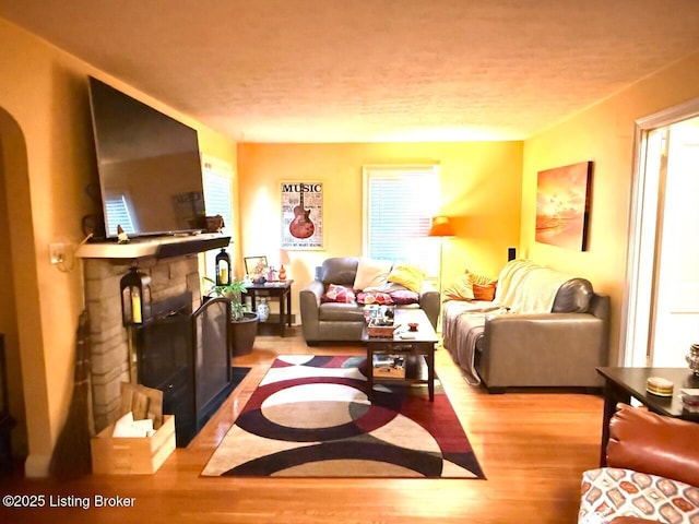 living room featuring light wood finished floors, a fireplace, arched walkways, and a textured ceiling