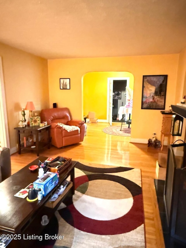 living area with baseboards, arched walkways, and wood finished floors