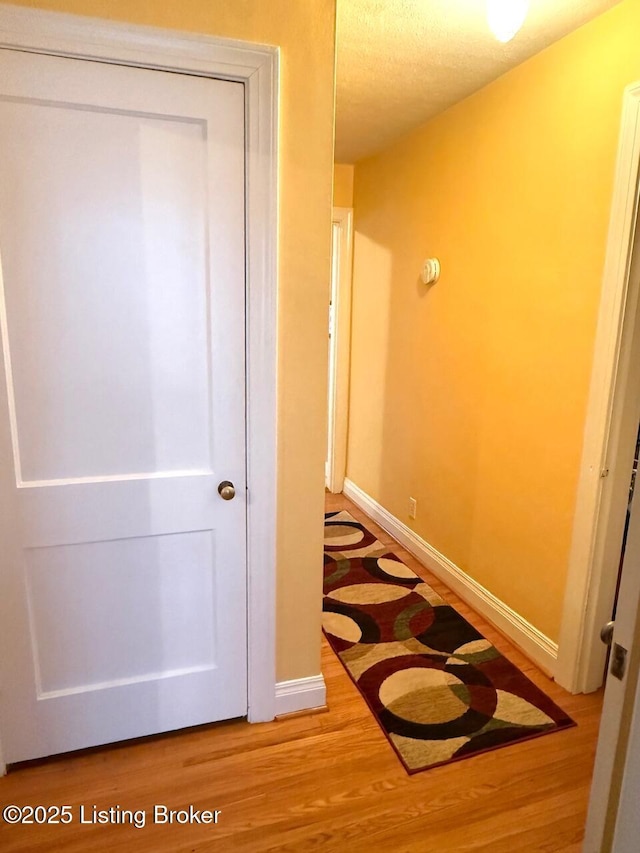 hallway featuring a textured ceiling, wood finished floors, and baseboards