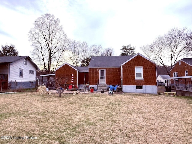 back of house with entry steps, brick siding, a lawn, and fence