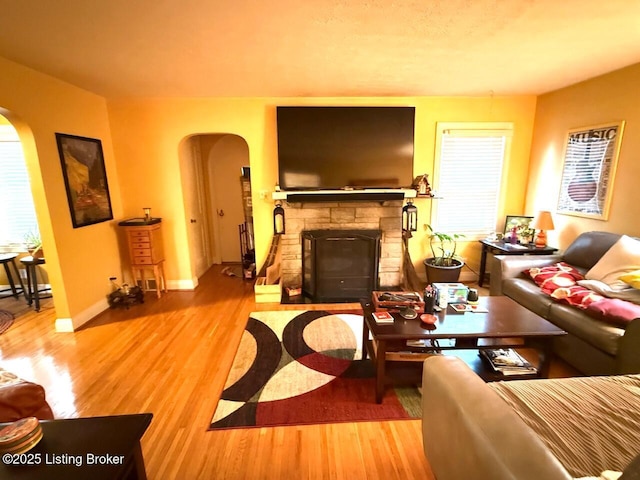 living room featuring arched walkways, a stone fireplace, wood finished floors, and a healthy amount of sunlight