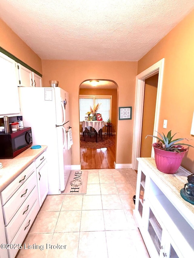 kitchen featuring light tile patterned floors, arched walkways, freestanding refrigerator, light countertops, and white cabinetry