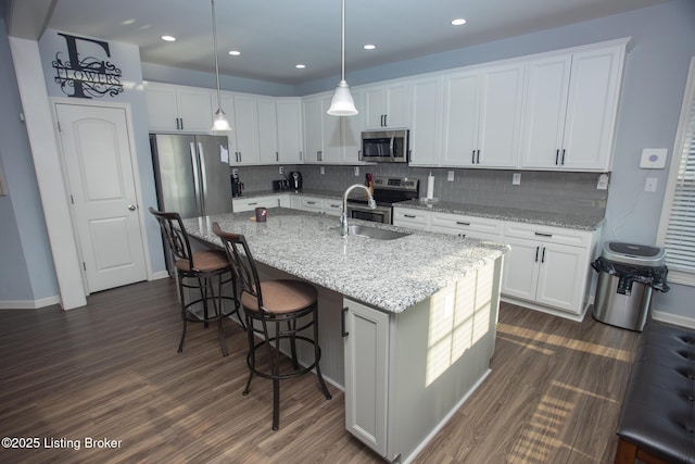 kitchen with white cabinetry, hanging light fixtures, a center island with sink, stainless steel appliances, and light stone countertops