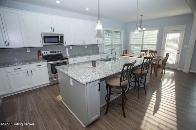 kitchen with pendant lighting, white cabinets, a kitchen island with sink, stainless steel appliances, and dark wood-type flooring