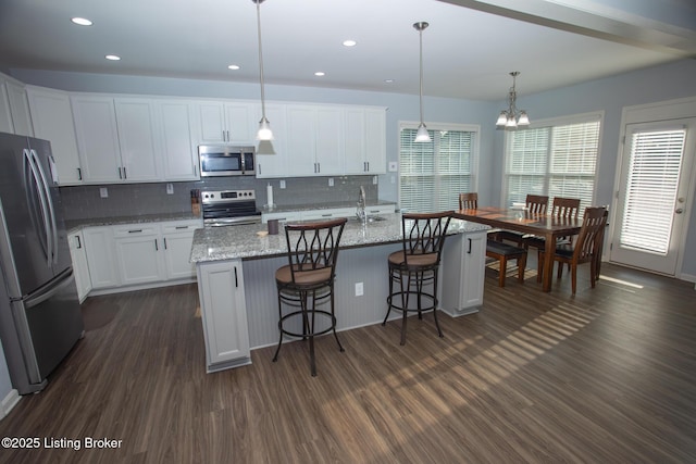 kitchen with hanging light fixtures, stainless steel appliances, an island with sink, white cabinets, and dark hardwood / wood-style flooring