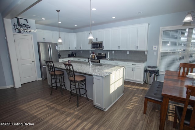 kitchen featuring white cabinetry, stainless steel appliances, a center island with sink, and pendant lighting