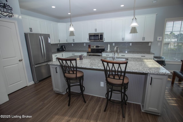 kitchen featuring stainless steel appliances, white cabinetry, hanging light fixtures, and a center island with sink