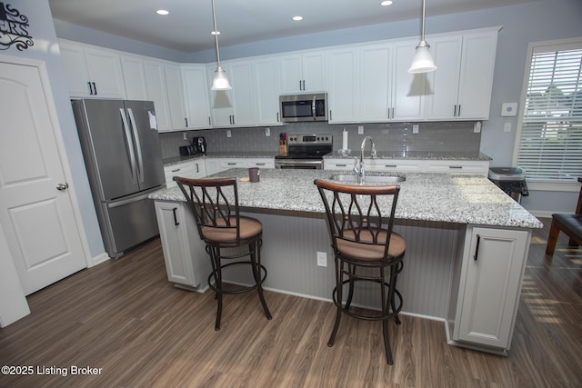 kitchen featuring stainless steel appliances, white cabinetry, hanging light fixtures, and a kitchen island with sink