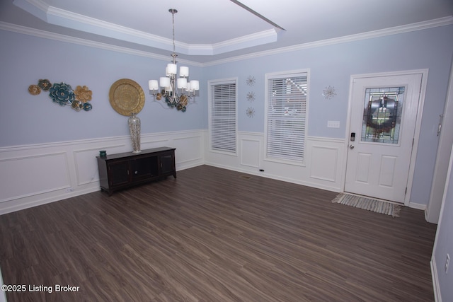 unfurnished dining area featuring crown molding, a chandelier, a raised ceiling, and dark wood-type flooring