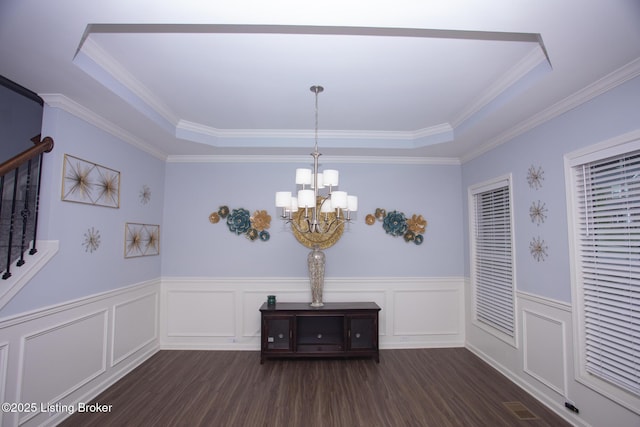 unfurnished dining area with ornamental molding, dark hardwood / wood-style floors, a notable chandelier, and a tray ceiling