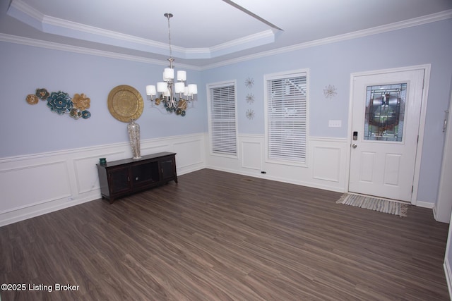 unfurnished dining area featuring crown molding, an inviting chandelier, a tray ceiling, and dark wood-type flooring