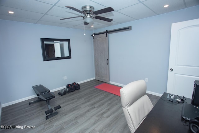 unfurnished office with ceiling fan, a paneled ceiling, wood-type flooring, and a barn door