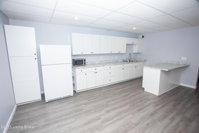 kitchen featuring white refrigerator, light stone countertops, white cabinets, and kitchen peninsula