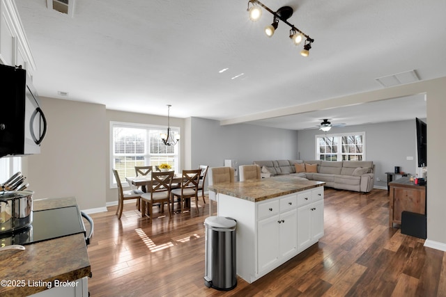 kitchen with an inviting chandelier, hanging light fixtures, white cabinets, dark hardwood / wood-style flooring, and dark stone counters