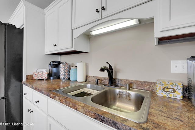 kitchen with white cabinetry, black fridge, and sink