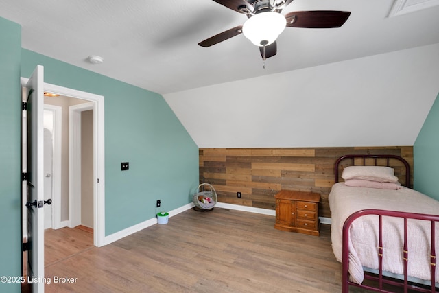 bedroom featuring ceiling fan, lofted ceiling, wooden walls, and light wood-type flooring