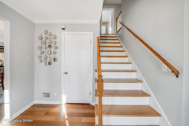 stairway with crown molding and wood-type flooring