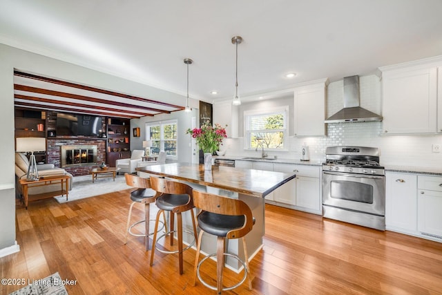 kitchen featuring white cabinetry, sink, hanging light fixtures, wall chimney range hood, and stainless steel gas range