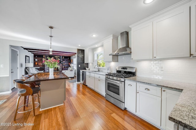 kitchen featuring appliances with stainless steel finishes, white cabinets, a center island, light stone counters, and wall chimney range hood