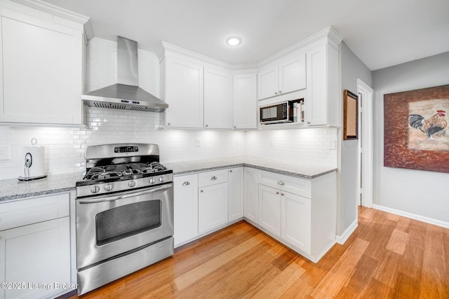 kitchen featuring light stone counters, white cabinets, stainless steel gas stove, and wall chimney range hood