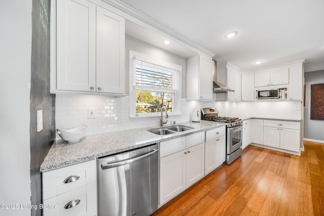 kitchen featuring sink, wall chimney range hood, light hardwood / wood-style flooring, appliances with stainless steel finishes, and white cabinets