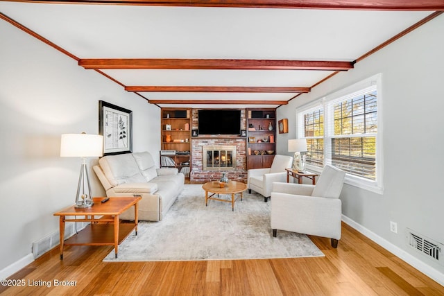 living room featuring hardwood / wood-style floors, crown molding, a fireplace, and beamed ceiling