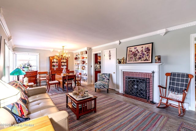 living room featuring built in shelves, crown molding, a chandelier, a fireplace, and hardwood / wood-style floors