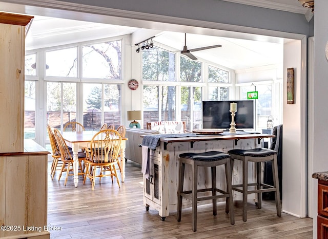 kitchen featuring a kitchen bar, vaulted ceiling, light hardwood / wood-style flooring, ornamental molding, and ceiling fan