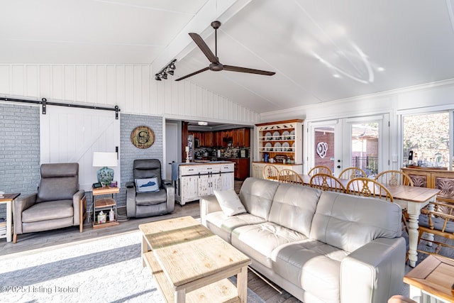 living room featuring french doors, wood walls, vaulted ceiling with beams, ceiling fan, and a barn door