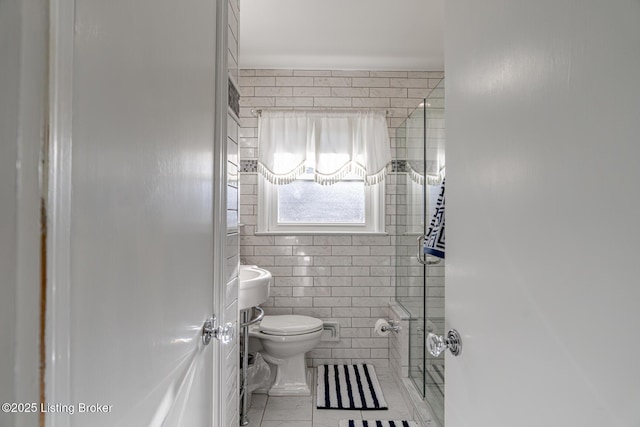 bathroom with tile patterned flooring, a shower with door, tile walls, and toilet