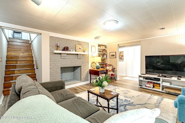 living room with crown molding, built in features, hardwood / wood-style floors, and a brick fireplace