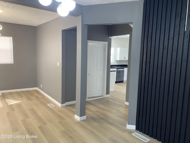 interior space with a textured ceiling, light wood-style flooring, visible vents, and baseboards