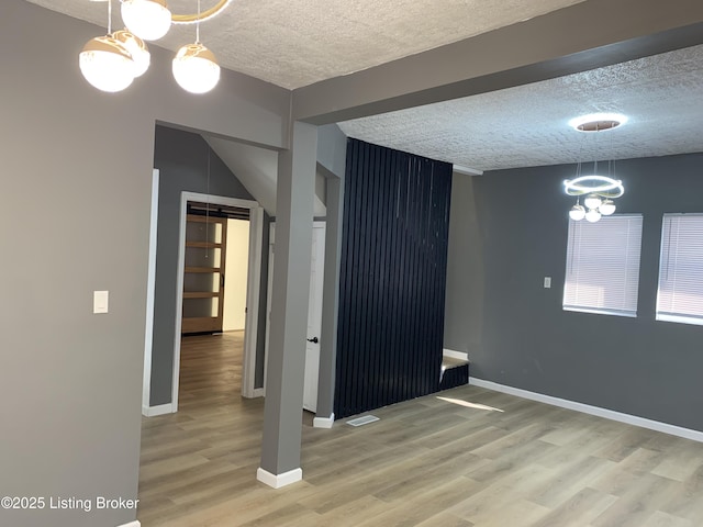 unfurnished room featuring visible vents, baseboards, wood finished floors, an inviting chandelier, and a textured ceiling