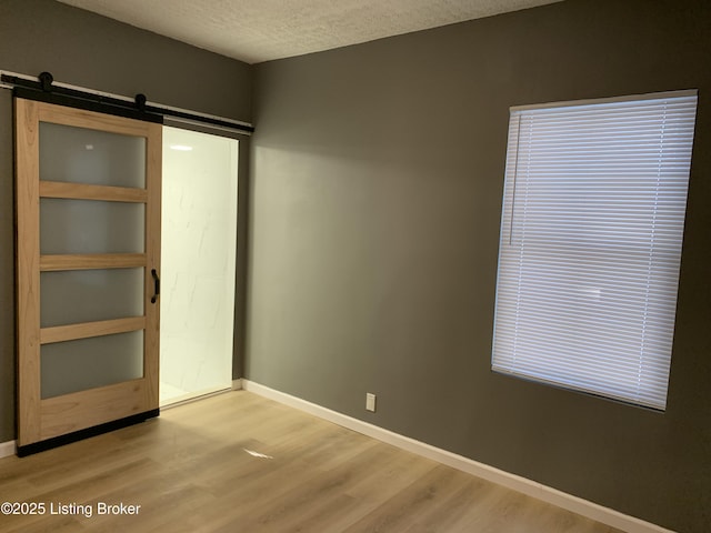 empty room with a textured ceiling, a barn door, light wood-type flooring, and baseboards