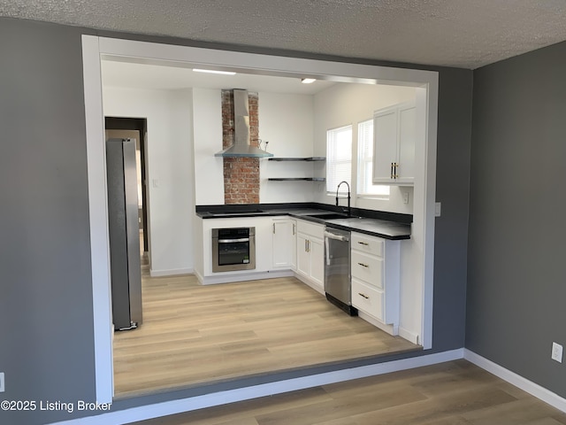 kitchen featuring wall chimney range hood, appliances with stainless steel finishes, light hardwood / wood-style floors, a textured ceiling, and white cabinets