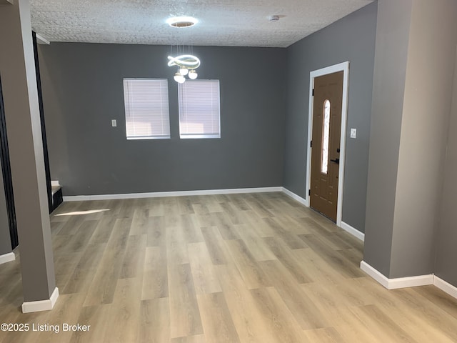 spare room featuring a chandelier, a textured ceiling, and light wood-type flooring